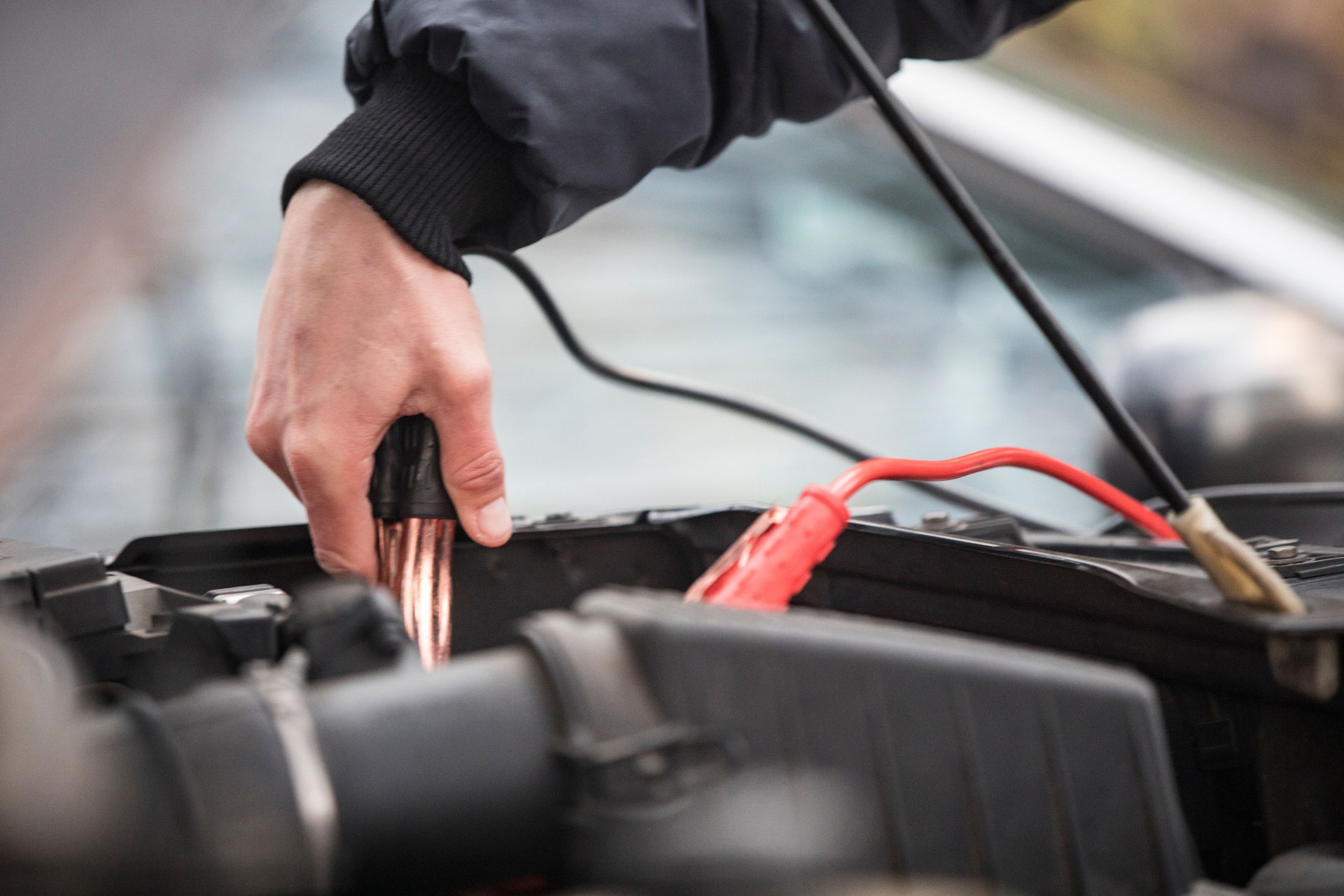 Young Adult Man Using Jumper Cables To Jump Start Engine of a Car - Stock Photo