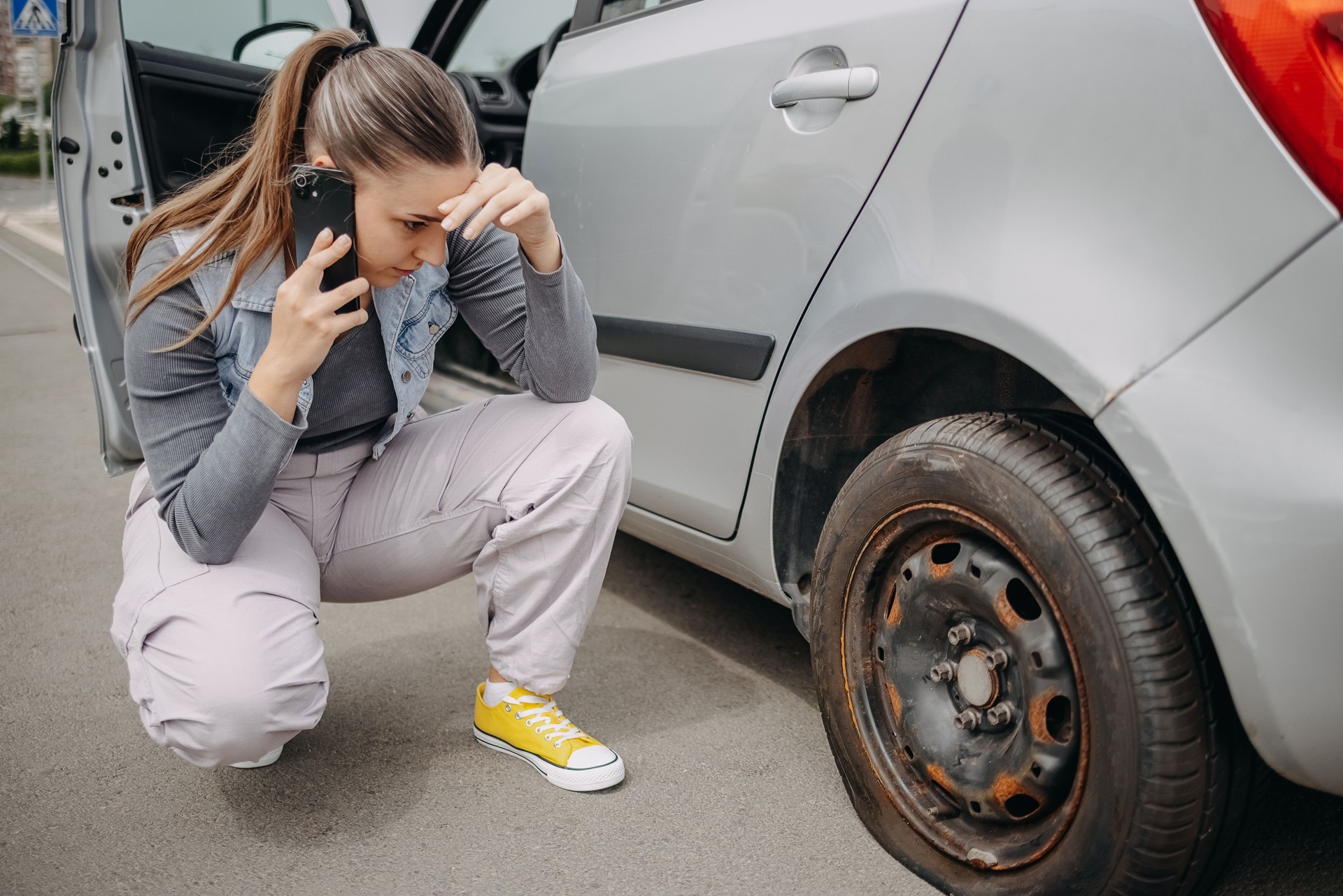 Woman having a flat tyre on the road and using mobile phone to ask for assistance